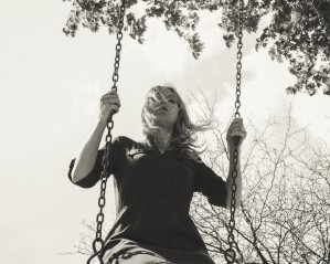 Ground view vintage black and white portrait of a young blonde woman on a swing by a windy day